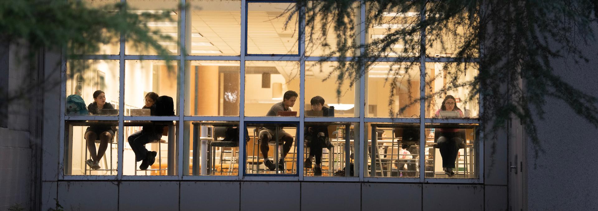 Students studying in the library, photographed from outside through a window