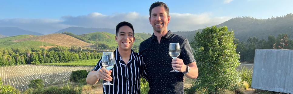 Two students hold up wineglasses outside in a vineyard