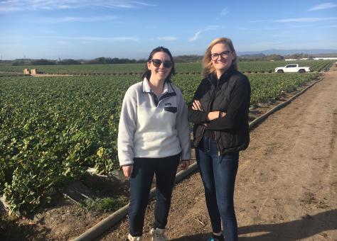 Two women standing on a dirt road next to a field