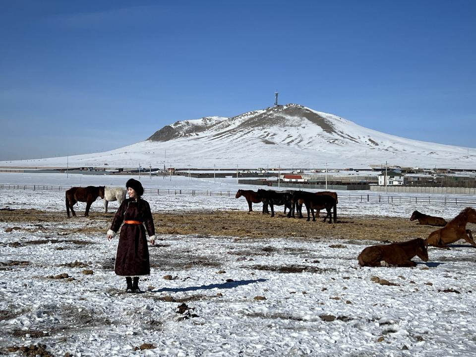 Sodontuya Nerguidavaa standing in a snowy mountainscape, surrounded by horses