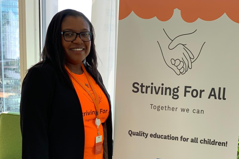 Genevieve Ngambia standing next to a sign with the name of the nonprofit she founded