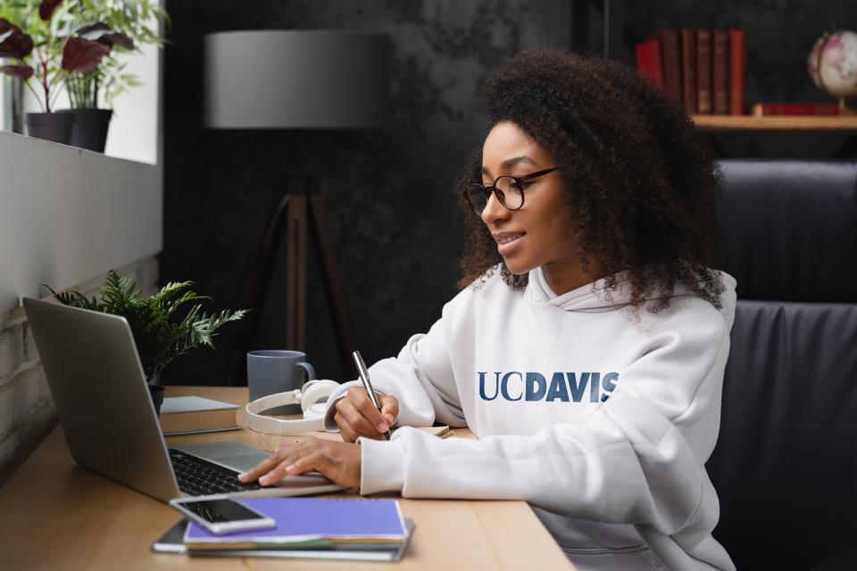 Woman sitting at laptop wearing a UC Davis sweatshirt